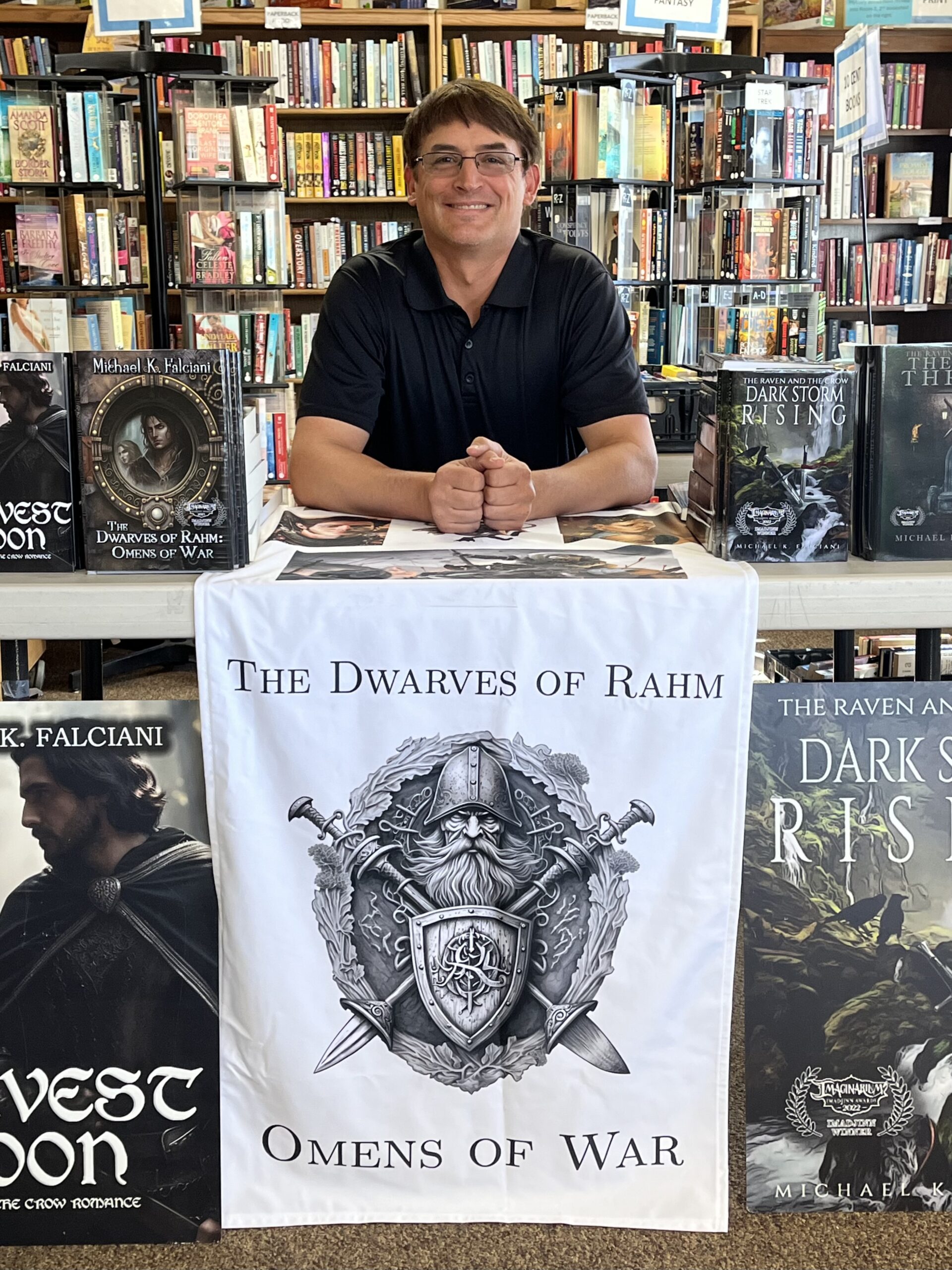 A photo of author Michael Falciani proudly sitting in front of his books with bookshelves behind.